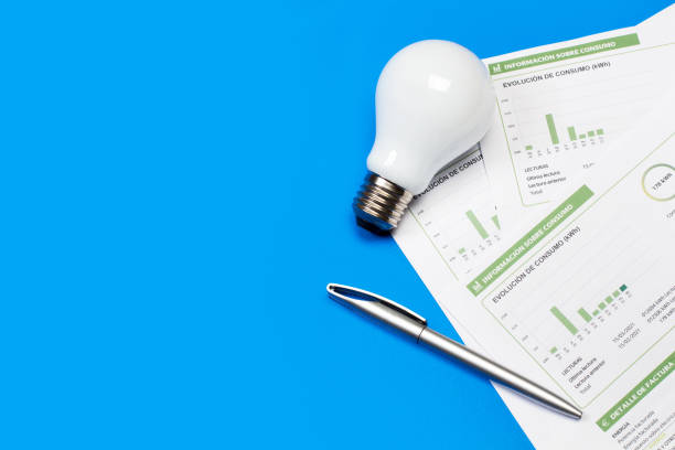 A lightbulb and an electricity bill on a blue background A lightbulb and an electricity bill on a blue background in a top view low photos stock pictures, royalty-free photos & images