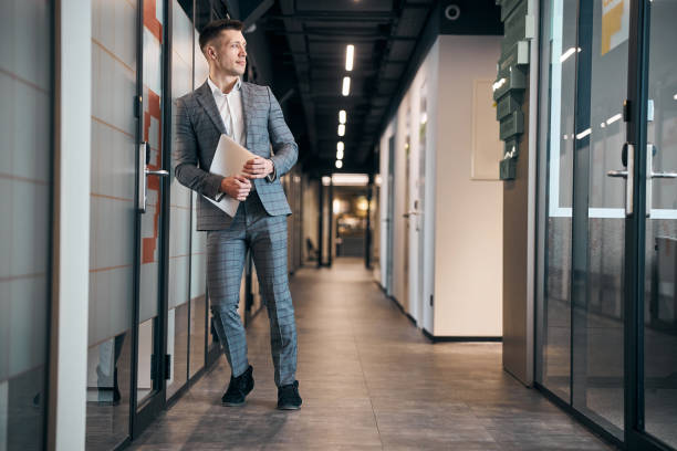 istock Handsome young man with laptop standing in office corridor 1313489157