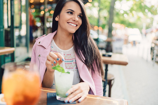 Smiling woman drinking mojito at sidewalk cafe
