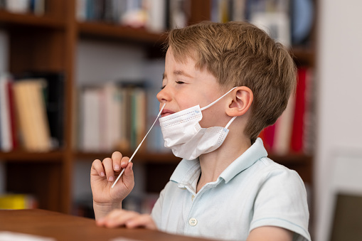 4 year pre-school boy introduces a corona test swab into his nose as he carries out a corona self test