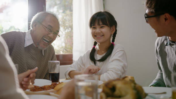 szczęśliwa azjatycka rodzina zjeść śniadanie razem. wesoły rodzice, dziadek i urocza córka jedzą razem śniadanie na stole w domu. wspaniała chwila rodzina - dining table child grandparent grandchild zdjęcia i obrazy z banku zdjęć