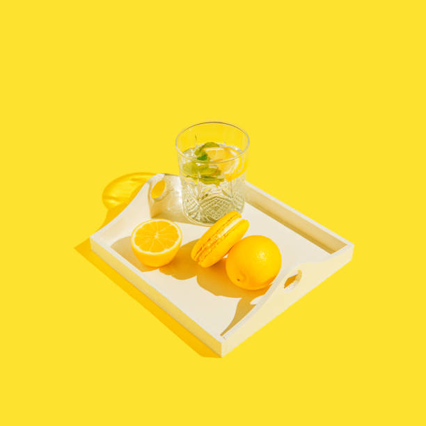 Yellow macaroon with lemons on white tray and glass of lemonade on sulit background . Summer refreshment concept.