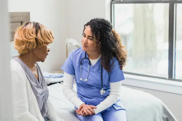 Photo of Caring nurse listens to senior patient during home visit