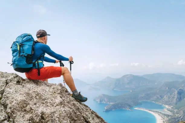 Young backpacker man sitting on cliff and enjoying the Mediterranean Sea bay at Oludeniz during Lycian Way trekking walk. Famous Likya Yolu Turkish route. Active sporty people vacations concept image