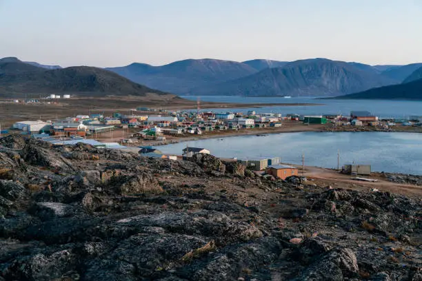 Photo of Dusk in a harsh arctic landscape with bare hills and ocean. Overlook of Inuit settlement of Qikiqtarjuaq, Broughton Island, Nunavut