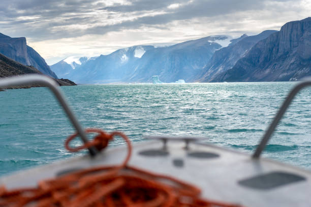 fiord north pangnirtung ze stromymi klifami i górami lodowymi unoszącymi się w wodzie w cieśninie davisa. arktyczna pustynia z małej łodzi. dramatyczne światło. - baffin island zdjęcia i obrazy z banku zdjęć