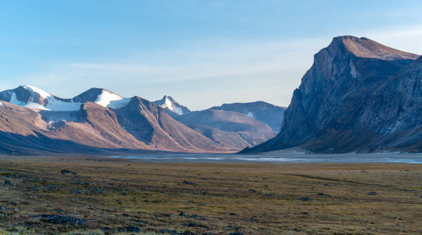 Monumental, wild arctic valley during sunset. Tall peaks with snow on top and river bed below. Duskfall at Akshayuk pass, Baffin Island, Canada. stock photo