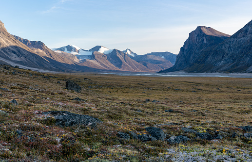 Monumental, wild arctic valley during sunset. Tall peaks with snow on top and river bed below. Duskfall at Akshayuk pass, Baffin Island, Canada. The north.