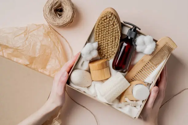 Photo of Beauty subscription Box preparation. Female hands holding gift box with natural skincare products, body brush, shampoo, soap, moisturizer.