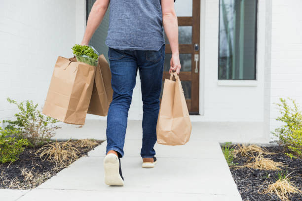 Man briskly delivers three bags of groceries to home The unrecognizable mid adult man briskly carries three paper bags full of groceries to the front door of the house. carrying stock pictures, royalty-free photos & images