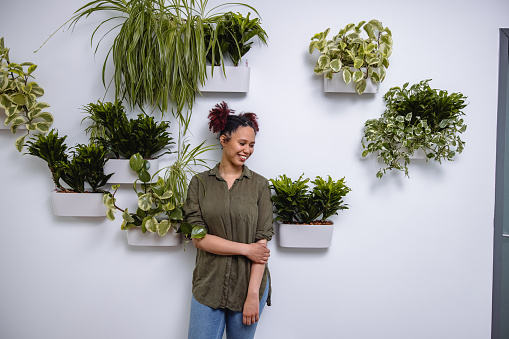 Portrait of a beautiful mixed race businesswoman in 20's smiling. Standing in a modern office in front of a plant wall.