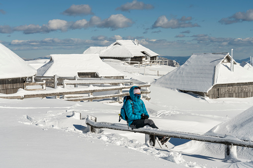 Women in idyllic landscape in Velika planina, Big Pasture Plateau in Slovenia, Europe, wooden pasture cottage covered with lot of snow against clear blue sky.