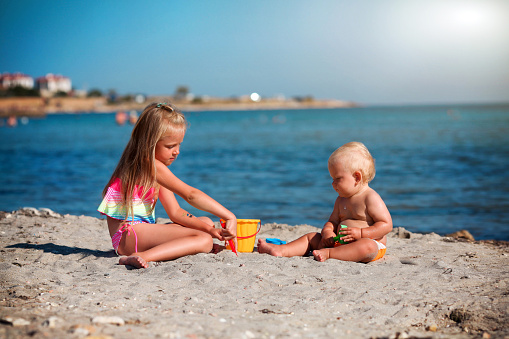 Children play on the beach. Summer water fun for the family. Boy and girl with toy buckets and a shovel on the seashore. Relax in the ocean with a baby and toddler.