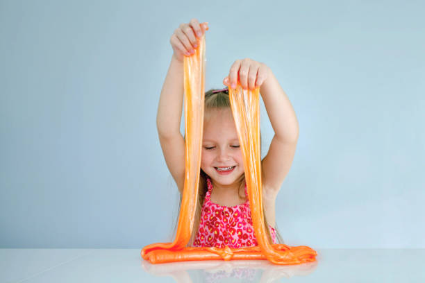 Cute funny girl play with orange slime. Kid squeeze and stretching toy slime.Copy space. Cute funny girl play with orange slime. Kid squeeze and stretching toy slime.Copy space. slimy stock pictures, royalty-free photos & images