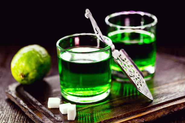 absinthe in glass with lemon slices on dark background with white sugar doses of absinthe with brown sugar cubes. distillate of absinthe in a glass and lemon, stainless steel spoon isolated on black background absinthe spoon stock pictures, royalty-free photos & images