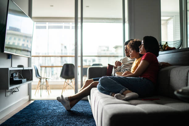 famille regardant la tv et mangeant le maïs éclaté à la maison - regarder la télévision photos et images de collection