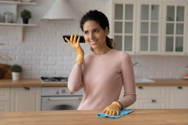 istock Young latina female cleaning modern kitchen hold phone use loudspeaker 1313525154