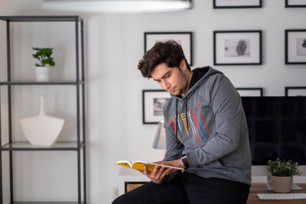 istock Young man reading book in the library 1313532800