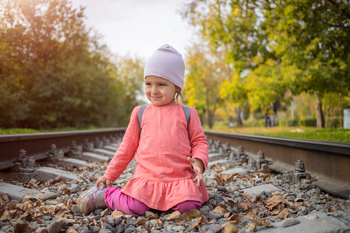 little girl sitting on the railroad tracks.  toddler plays on railroad in forest