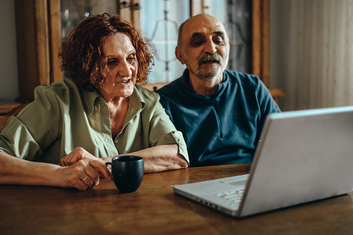 Senior couple using a laptop while relaxing at home and drinking coffee together