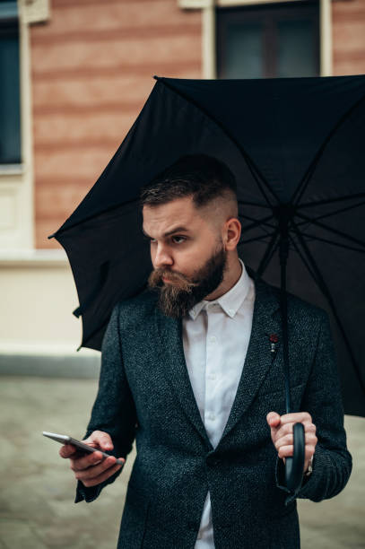 istock Businessman using a smartphone and holding a black umbrella 1313535214