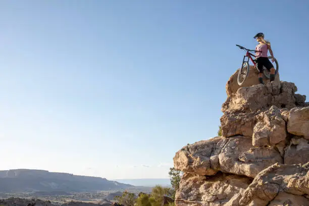 Photo of Female mountain biker hikes up mountain ridge at sunrise