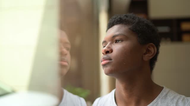 Teenager boy looking through window contemplating at home