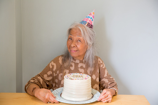 Elderly Asian senior woman wearing a party hat celebrating her birthday with a cake