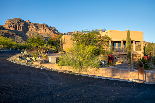 Contemporary adobe home with desert landscaping near sunset with mountain backdrop in Tucson, AZ.