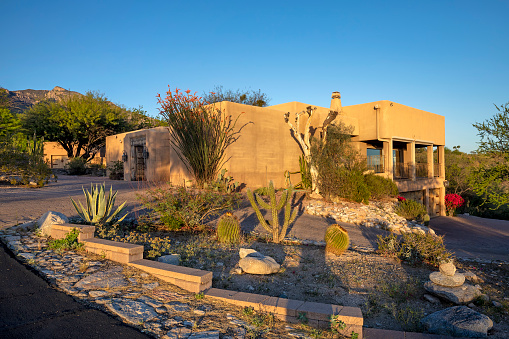 Contemporary adobe home with desert landscaping near sunset with mountain backdrop in Tucson, AZ.