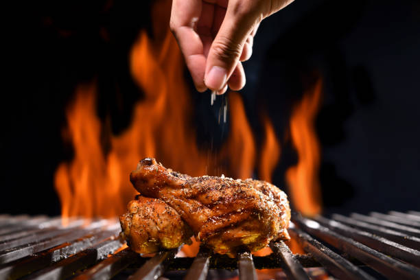 불타는 그릴에 구운 닭 다리에 소금과 향신료를 손으로 뿌립니다. - chicken roast 뉴��스 사진 이미지