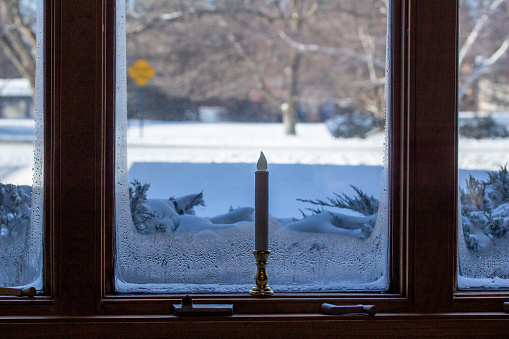 Close-up abstract view of a modern style ice lined window with a holiday candle stick, looking out onto a snow covered yard in winter.
