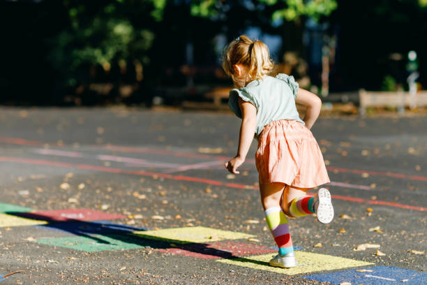 아스팔트에 화려한 분필로 그려진 홉스카치 게임을 하는 귀여운 어린 유아 소녀. 화창한 날에 는 야외에서 놀이터에서 뛰어 다니는 활동적인 어린 아이. 어린이를위한 여름 활동. - little girls sidewalk child chalk 뉴스 사진 이미지