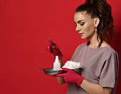 Young pretty brunette woman nurse doctor in red latex gloves holds tools on tray and medical scissors in hand