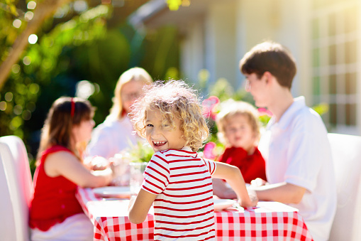 Family eating outdoors. Garden summer fun. Barbecue in sunny backyard. Grandmother and kids eat lunch in outdoor deck. Parents and children enjoy bbq. Boy and girl with mother.