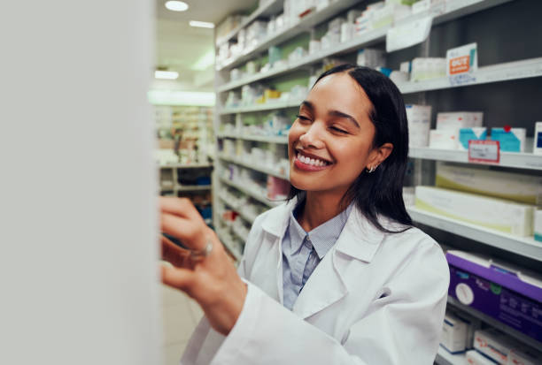 alegre farmacéutica que usa bata de laboratorio en busca de medicina en estantería en químico - pharmacy medicine pharmacist storage room fotografías e imágenes de stock