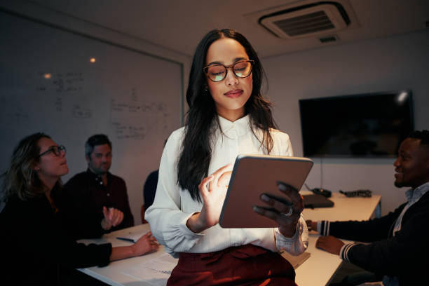 portret bizneswoman za pomocą cyfrowego tabletu z jej zespołem siedzącym przy biurku w sali konferencyjnej - standing digital tablet adult beautiful zdjęcia i obrazy z banku zdjęć
