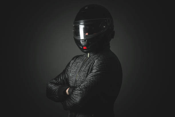 Motorbiker. Serious motorbiker in a helmet with a crossed arms is standing on the dark background. race car driver stock pictures, royalty-free photos & images