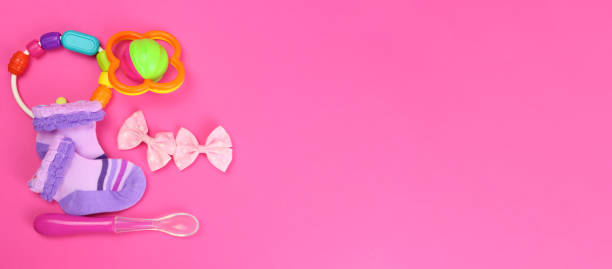 istock Baby clothes, rattles, feeding spoon on pink background. Horizontal banner. Copy space for text 1313592766
