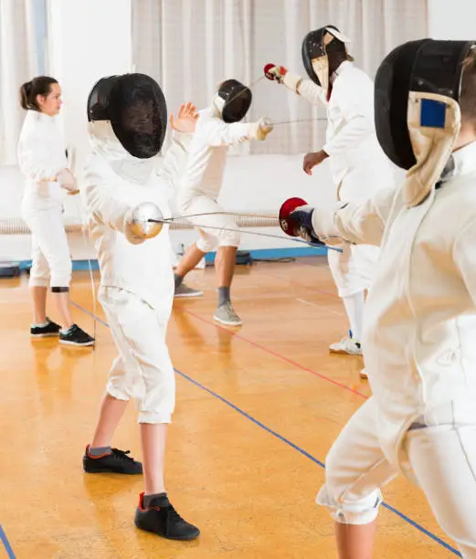Portrait of kids and adults fencers with instructor engaged in fencing in training room