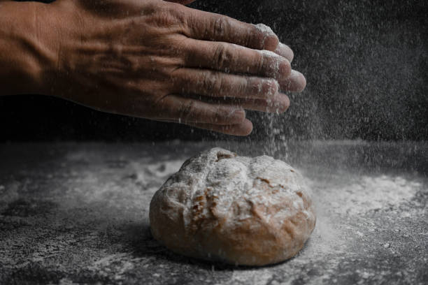 istock Baker clap hands with flour splash on fresh bread.Bakery, cooking concept lifestyle on black background. 1313596219