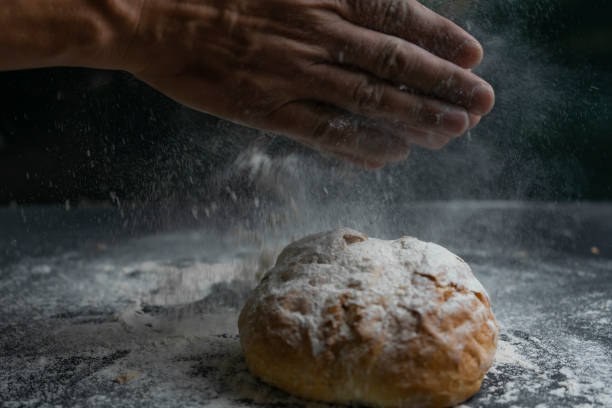 istock Chefs hands scattering flour and splash on rustic bread.Concept of baking ,cooking ,recipe in dark black background. 1313596246