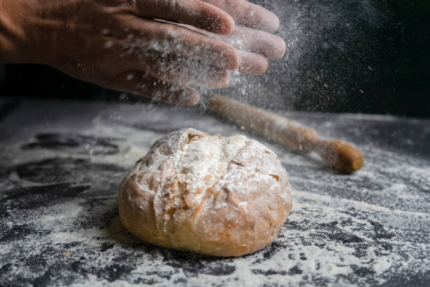 istock Baker clap hands with flour splash on fresh bread.Bakery concept lifestyle with rolling on floury black background. 1313596275