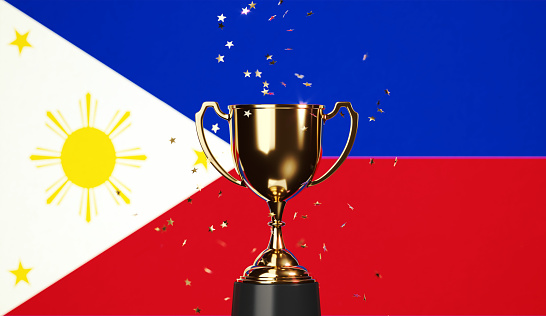Star shaped gold confetti falling onto a gold cup sitting over Philippines flag background. Horizontal composition with copy space. Front view. Championship concept.