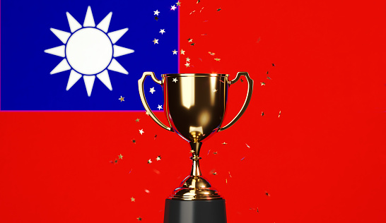 Star shaped gold confetti falling onto a gold cup sitting over Taiwanese flag background. Horizontal composition with copy space. Front view. Championship concept.