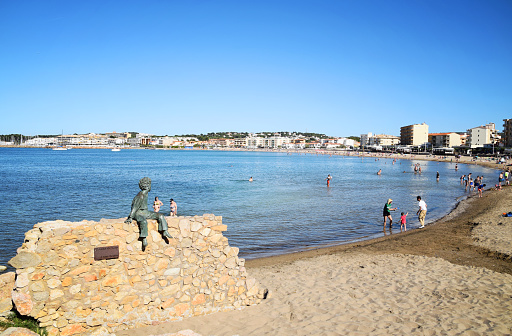 L'Escala, Spain - June 01 2019: City beach with people going for a swim. Beach surrounded by the town's buildings and houses. Beach in the seaside town L'Escala in Spain.