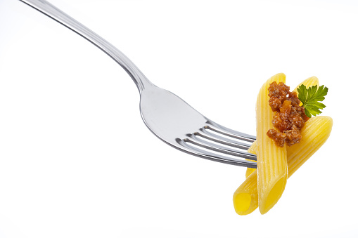 Penne pasta with bolognese meat sauce and parsley leaf on a fork isolated on white background. Eating classic italian cuisine.