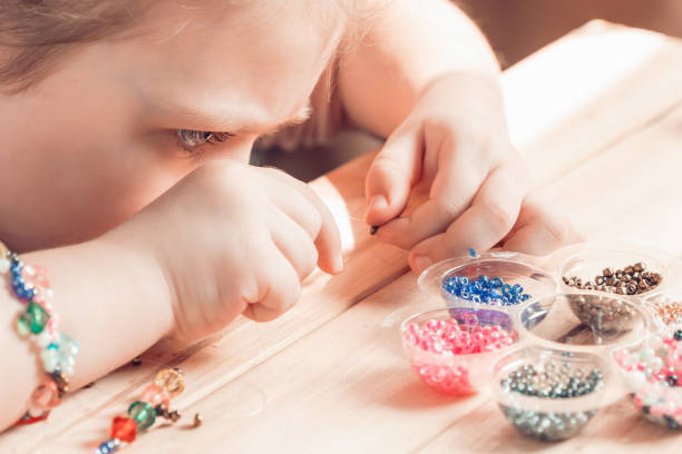 istock A little girl is engaged in needlework, making jewelry with her own hands, stringing multi-colored beads on a thread 1313603324