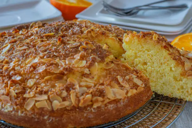 Delcious fresh baked almond orange cake served on a kitchen table with plates and forks in the background. Closeup view