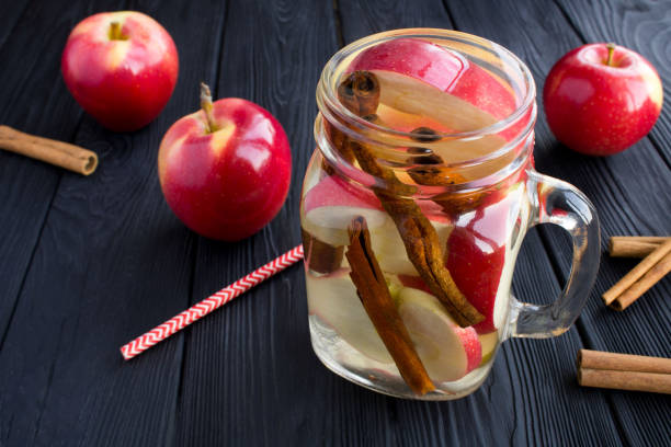 água infundida ou desintoxicação com maçã e canela no vidro no fundo de madeira preta. close-up. - apple red fruit water - fotografias e filmes do acervo